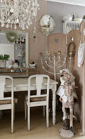 Old dolls on rocking horse and candlestick next to white painted wooden table, above chandelier