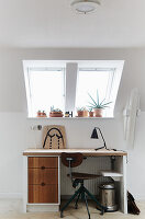 Workplace under sloped ceiling with vintage desk and houseplants on the windowsill