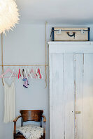 Garderobe mit Kleiderbügeln, weißem Shabby-Chic-Schrank und Holzstuhl