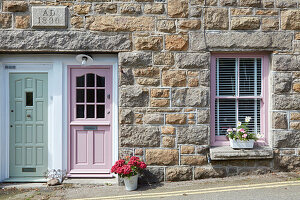 Traditional stone building with pink door and shutters and flower pots