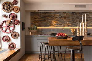 Teak breakfast bar in open-plan kitchen with slate-clad wall; old wheels and cogs on wall in foreground