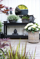 Schwarzer Tisch mit Pflanzen, darüber Spiegel vor weißer Fassade aus Holz