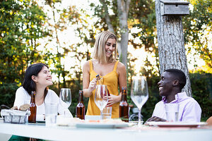 Freunde bei einem sommerlichen Abendessen im Garten öffnen eine Flasche Wein