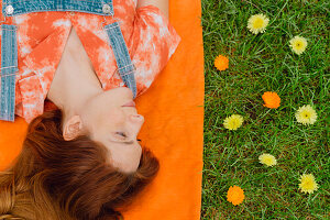 Beautiful redhead woman lying on picnic blanket by flowers at back yard