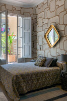 Doppelbett und Goldrahmenspiegel an Wand mit gemusterter Tapete, im Schlafzimmer mit Terrassenzugang