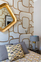 Queen sized bed and gold-framed mirror on a wall with patterned wallpaper