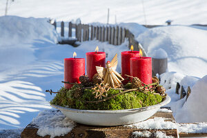 Advent wreath with red candles and moss in an enamel bowl in the garden
