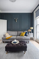 Grey sofa and button-tufted ottoman in living room with grey walls and moulding