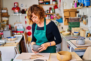 Concentrated middle aged female potter shaping clay workpiece pot in professional pottery studio