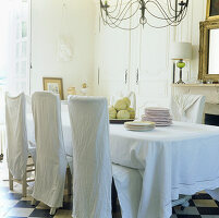 Dining chairs dressed with linen slip covers and an antique linen sheet is draped over the table