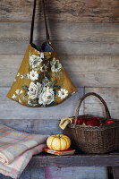 Rustikale Holzvertäfelung mit einer Hängetasche, einer Bank mit Kürbissen, einer Decke und einem Korb mit roten Äpfeln