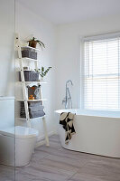 Bright bathroom with ladder shelf and free-standing tub in front of a window