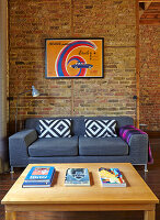 Wooden coffee table and grey upholstered sofa in room with brick walls