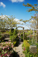Weg, gesäumt vom Tulpen, im Hintergrund Torbogen in sonnigem Garten