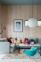 Modern living room with corner sofa, colourful cushions and wood panelling on the wall