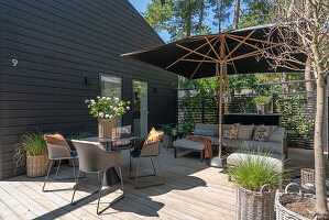 Terrasse mit Loungemöbeln, Sonnenschirm und Pflanzenkörben aus Rattan