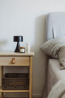 Bedside table with lamp and skincare products next to a bed