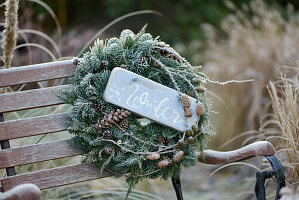 A winter wreath made of various fir sprigs, decorated with fir cones and a wooden sign with the inscription 'Winter'