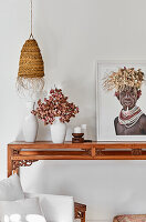Vase with dried flowers, candles, artwork on oriental wooden console, pendant lamp above it