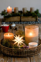 Christmas decoration with votive, candle, pine branches, and a star on a tray