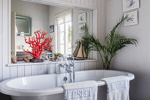 Red coral on shelf with large mirror above freestanding bath
