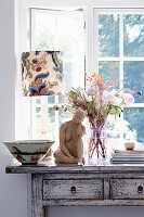 Shabby style table with a decorative ceramic bowl, table lamp, sculpture, and bouquet of flowers