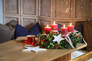 Adventskranz aus Stechpalmen mit roten Kerzen, einer Tasse und einem Buch auf Holztisch