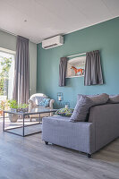 A grey upholstered sofa and a coffee table in a living room with a blue wall