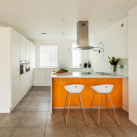 A breakfast bar with an orange front and bar stools in a white kitchen