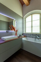 A washstand with an illuminated mirror above it and a bathtub in a bathroom
