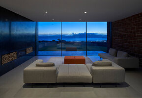 A minimalist living room with a window wall and a sea view at dusk