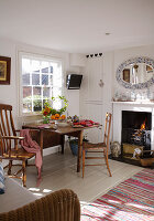 Windsor-Stuhl an einfachem Tisch im Landhaus-Esszimmer mit ovalem Mosaikspiegel über dem Kamin