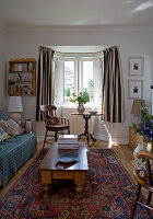 Alter Couchtisch aus Kiefernholz und gemusterter Teppich im  Wohnzimmer mit gestreiften Vorhängen