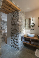 Wooden washbasin with countertop next to natural stone wall in bathroom ensuite