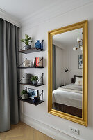 Großformatiger Wandspiegel mit Goldrahmen, daneben Wandregale im Schlafzimmer