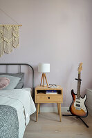 Bedside table between bed and guitar in bedroom