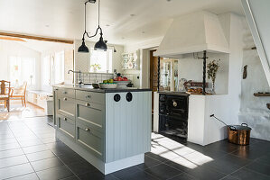 Bright, open-plan country-style kitchen, kitchen island in front of wood-burning stove