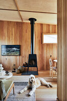 Gemütlicher Wohnraum mit Holzverkleidung und Kaminofen, Hund im Vordergrund