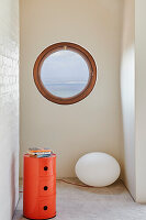 Orange-colored vintage cupboard and floor lamp in the room with porthole window
