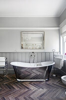 Freistehende Badewanne in Metallic-Look, darüber Spiegel im Badezimmer mit Bodenfliesen in Holzoptik
