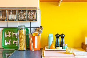 Storage containers and kitchen utensils in front of yellow wall