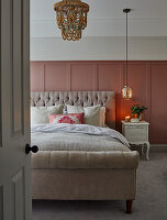 Elegant double bed with upholstered headboard in front of pink wall paneling