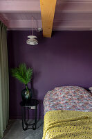 Sleeping area with purple wall, palm branch in vase and yellow knitted bedspread