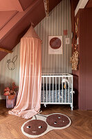 Children's room with sloping roof, wall design with striped wallpaper and rust-red colour, cot with canopy, carpet with cherries