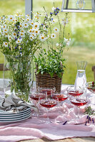 Wildflower bouquet with daisies in front of a laid table with aperitif glasses