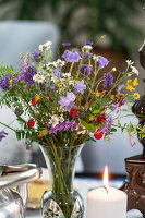Blumenarrangement mit Wildblumen und brennende Kerze auf dem Tisch