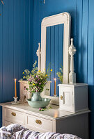 White dressing table with mirror and flower arrangement in front of blue wood panelling