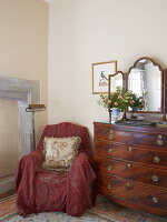 Armchair with red throw, antique chest of drawers and mirror in vintage bedroom