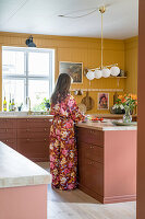 Woman in colorful clothing cooks in a kitchen painted yellow and red