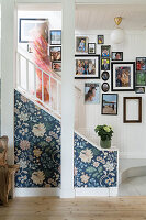 Staircase with floral wallpaper and family photos on a white wooden wall